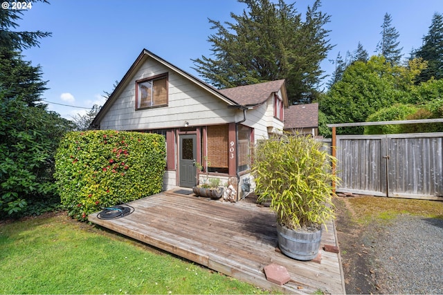 rear view of property featuring a yard, a deck, a shingled roof, and fence