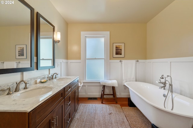 bathroom with a wainscoted wall, a sink, a freestanding tub, and double vanity