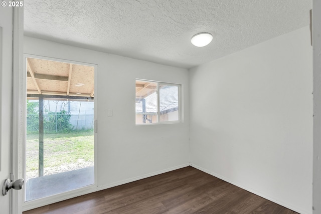 spare room featuring dark wood-type flooring, a textured ceiling, and baseboards