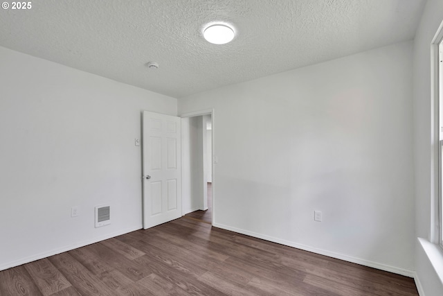 spare room featuring a textured ceiling, baseboards, wood finished floors, and visible vents