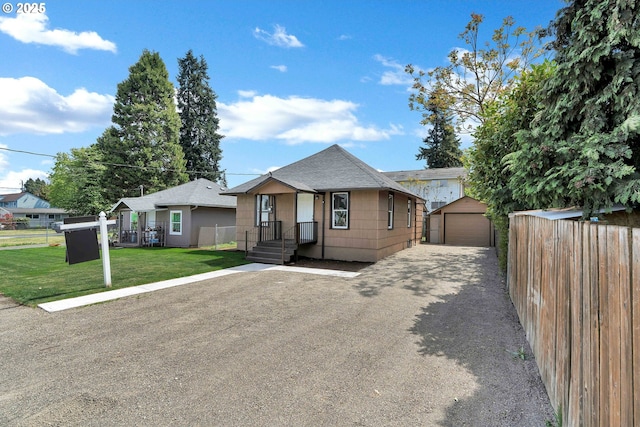 view of front of house with fence, a detached garage, an outbuilding, and a front lawn