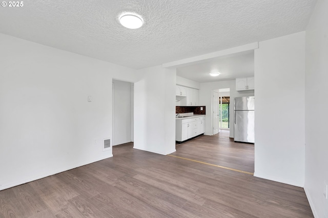 unfurnished living room featuring baseboards, a textured ceiling, dark wood-style floors, and visible vents