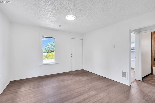 empty room featuring a textured ceiling, baseboards, wood finished floors, and visible vents