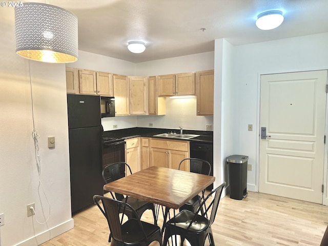 kitchen with light wood-style flooring, dark countertops, a sink, black appliances, and light brown cabinetry