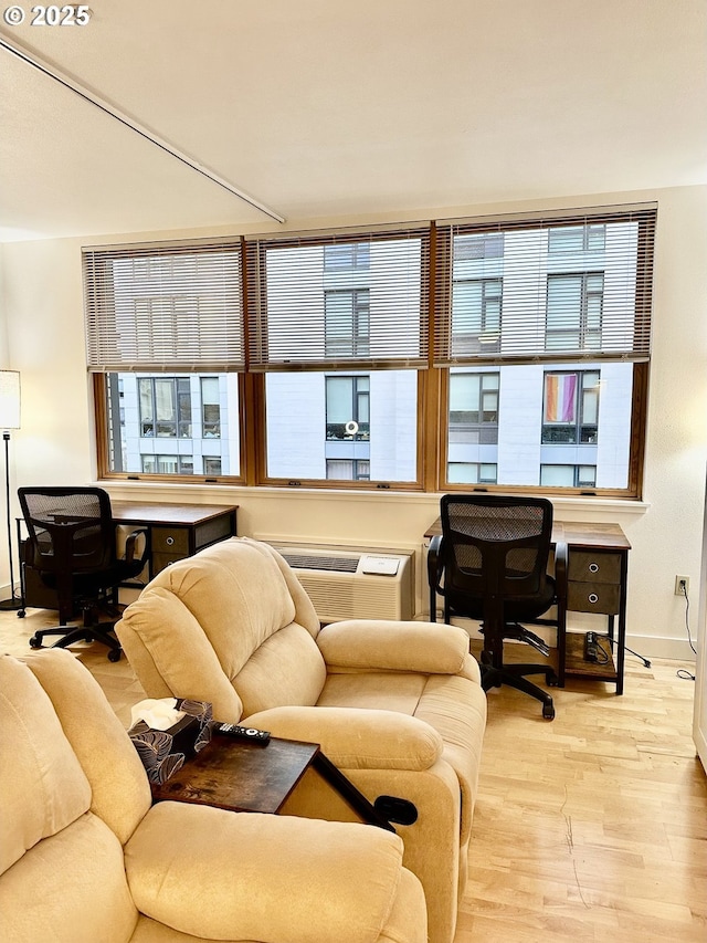 living area with baseboards, a wall unit AC, and light wood-type flooring
