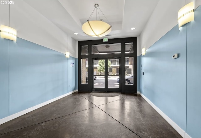 foyer entrance featuring baseboards, a tray ceiling, and finished concrete floors