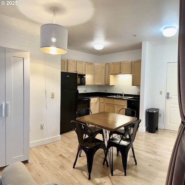kitchen featuring a sink, light wood-style flooring, light brown cabinets, dark countertops, and black appliances
