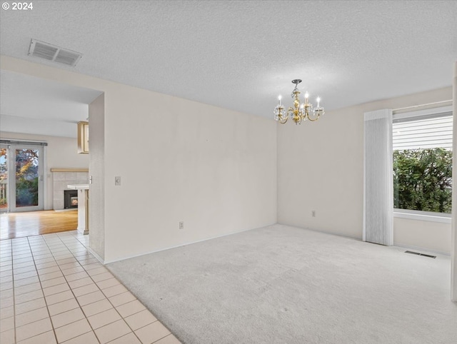 tiled empty room with a textured ceiling, a notable chandelier, and a tiled fireplace