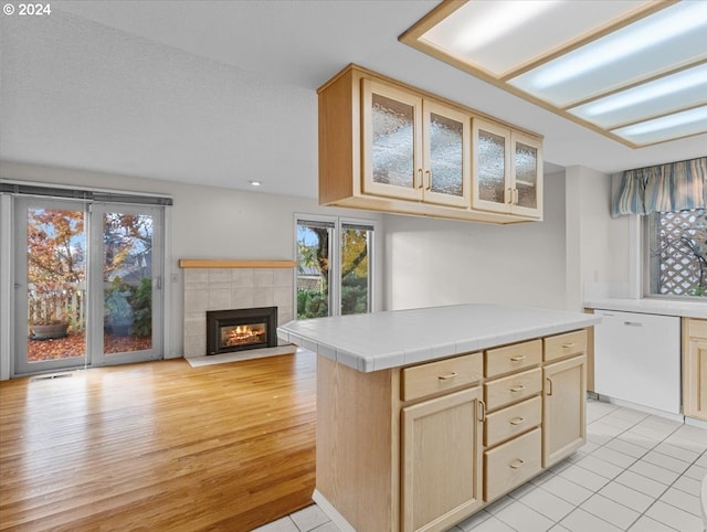 kitchen featuring tile countertops, dishwasher, light tile patterned floors, light brown cabinetry, and a tiled fireplace