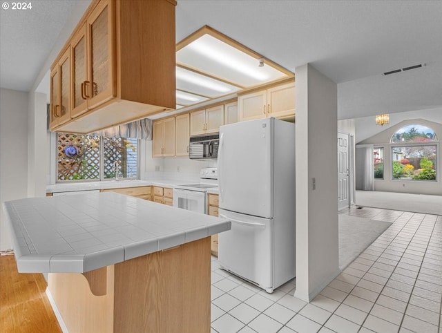 kitchen featuring a kitchen bar, light brown cabinets, white appliances, and tile counters