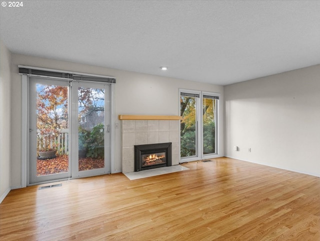 unfurnished living room with a tile fireplace, light hardwood / wood-style flooring, and a textured ceiling