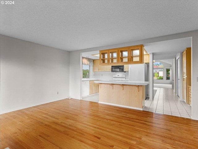 kitchen featuring a center island, light hardwood / wood-style floors, a textured ceiling, white appliances, and a kitchen bar