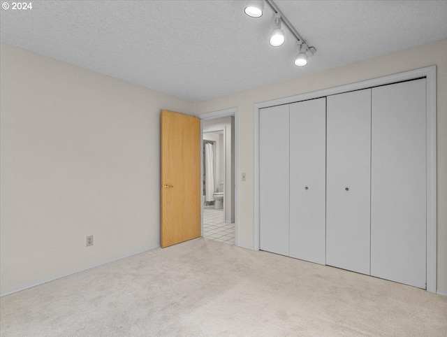 unfurnished bedroom with a textured ceiling, rail lighting, light colored carpet, and a closet