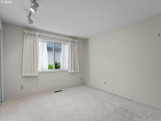 spare room featuring a textured ceiling, light colored carpet, and rail lighting