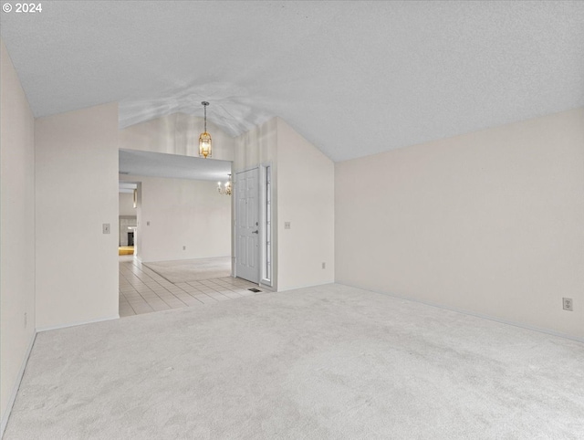 carpeted spare room with a textured ceiling, lofted ceiling, and an inviting chandelier