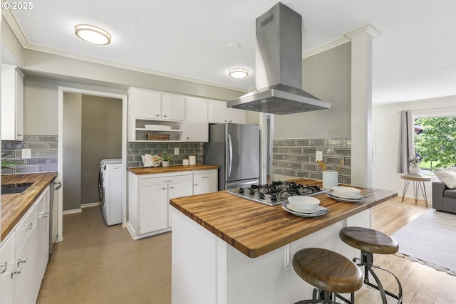 kitchen with butcher block countertops, island range hood, washer / dryer, stainless steel appliances, and white cabinetry