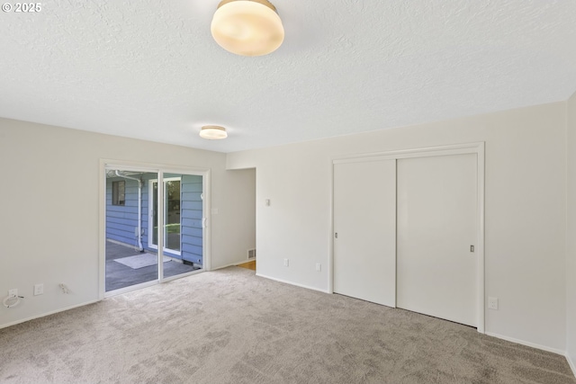 unfurnished bedroom with carpet, a closet, a textured ceiling, and access to exterior