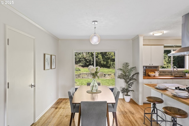 dining area with baseboards, plenty of natural light, ornamental molding, and light wood-style floors