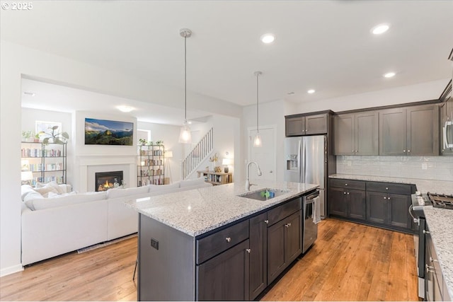 7010 SW Barr Ln, Tualatin, OR 97062 - kitchen featuring stainless steel appliances, light wood finished floors, light stone countertops, a warm lit fireplace, and open floor plan