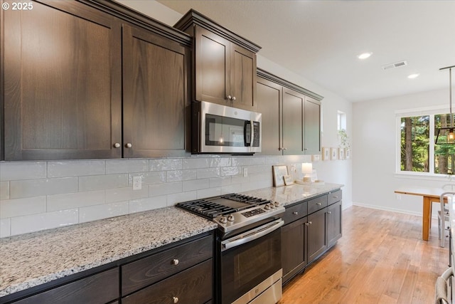 7010 SW Barr Ln, Tualatin, OR 97062 - kitchen featuring appliances with stainless steel finishes, tasteful backsplash, light wood-type flooring, dark brown cabinetry, and light stone countertops