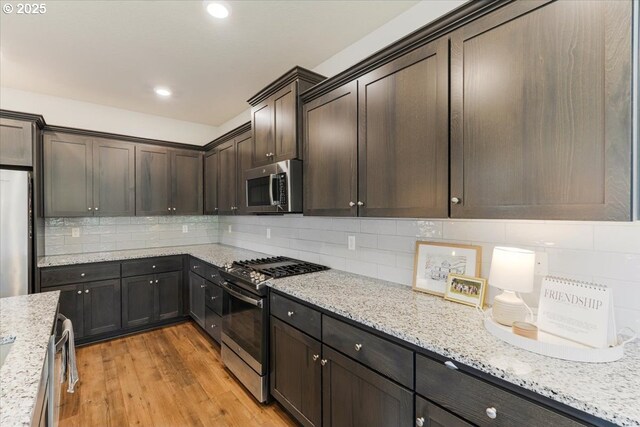 7010 SW Barr Ln, Tualatin, OR 97062 - kitchen featuring appliances with stainless steel finishes, decorative backsplash, dark brown cabinetry, light wood-style flooring, and light stone counters