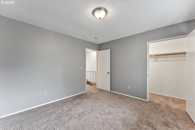 unfurnished bedroom featuring carpet, baseboards, a closet, a textured ceiling, and a walk in closet