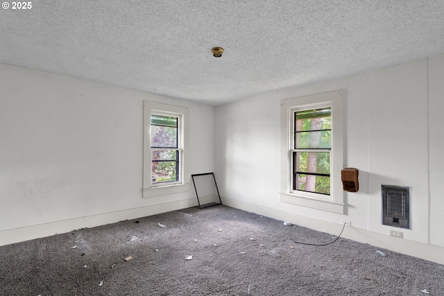 spare room with a textured ceiling, heating unit, and carpet