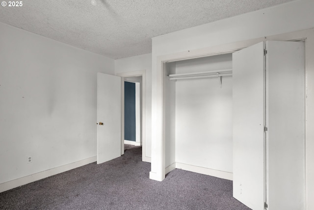 unfurnished bedroom with dark carpet, a textured ceiling, a closet, and baseboards