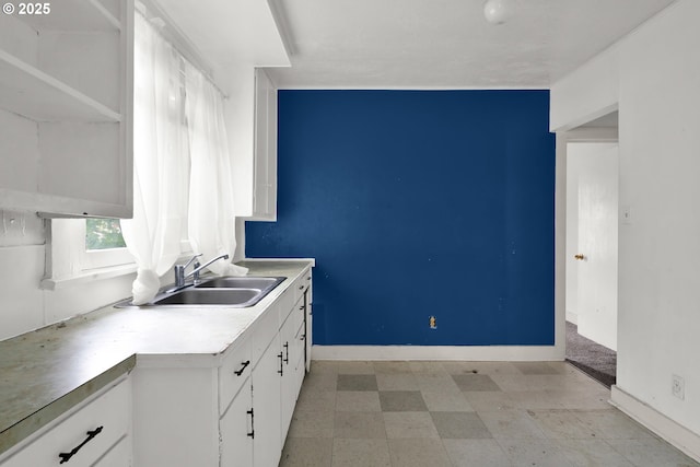 kitchen with a sink, white cabinetry, light floors, and baseboards