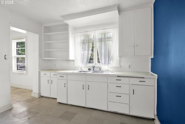 kitchen featuring a sink, open shelves, baseboards, and light countertops