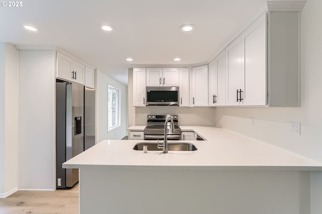 kitchen with a peninsula, recessed lighting, light countertops, a sink, and appliances with stainless steel finishes