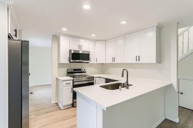 kitchen featuring appliances with stainless steel finishes, a sink, light countertops, a peninsula, and light wood-style floors