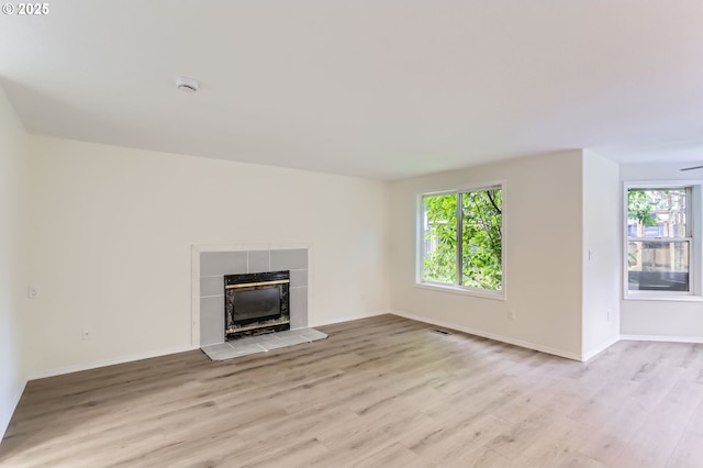 unfurnished living room with light wood-type flooring, a tile fireplace, and a wealth of natural light