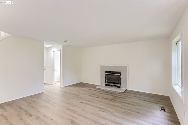 unfurnished living room with a tiled fireplace, baseboards, light wood finished floors, and visible vents