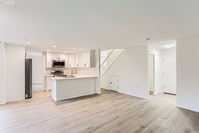 kitchen with appliances with stainless steel finishes, a sink, light countertops, white cabinets, and light wood-style floors