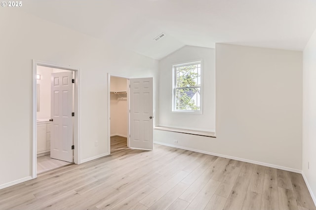 unfurnished bedroom with visible vents, lofted ceiling, light wood-style floors, baseboards, and a walk in closet