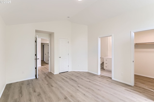 unfurnished bedroom with a walk in closet, light wood finished floors, baseboards, ensuite bathroom, and vaulted ceiling