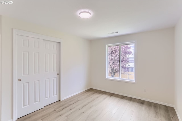 unfurnished bedroom with a closet, baseboards, visible vents, and light wood-type flooring