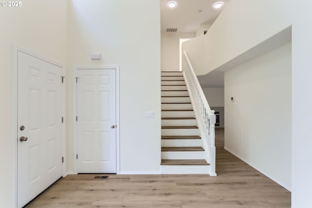 stairway featuring baseboards, a high ceiling, visible vents, and wood finished floors