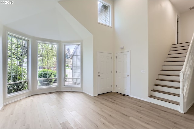 foyer entrance with light wood-style floors, baseboards, a high ceiling, and visible vents