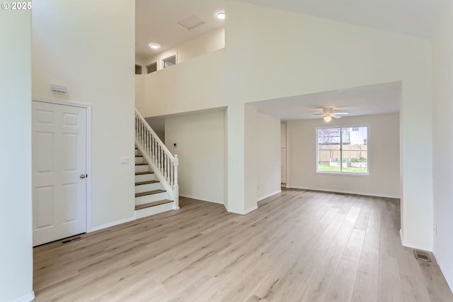 unfurnished living room with stairs, a ceiling fan, baseboards, wood finished floors, and a towering ceiling