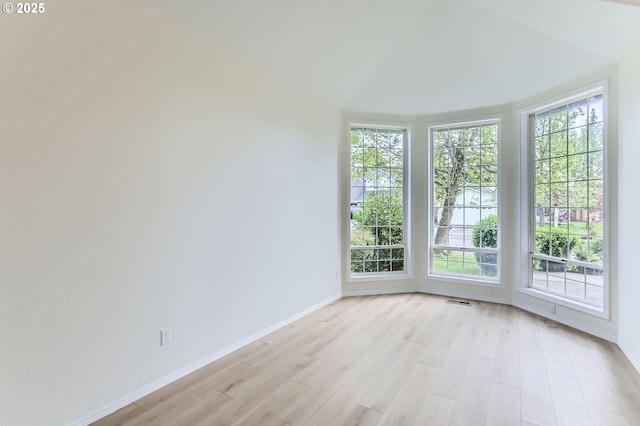 unfurnished room with baseboards, plenty of natural light, light wood finished floors, and lofted ceiling