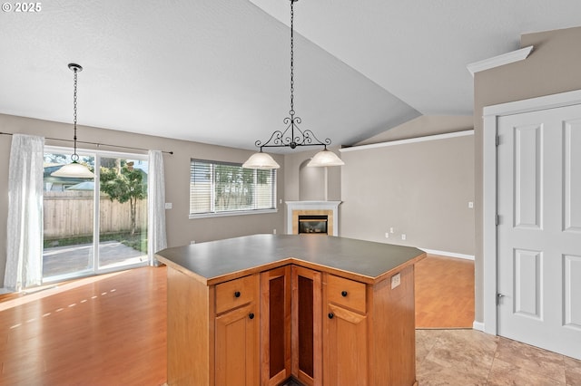 kitchen featuring a tiled fireplace, ornamental molding, a center island, and decorative light fixtures