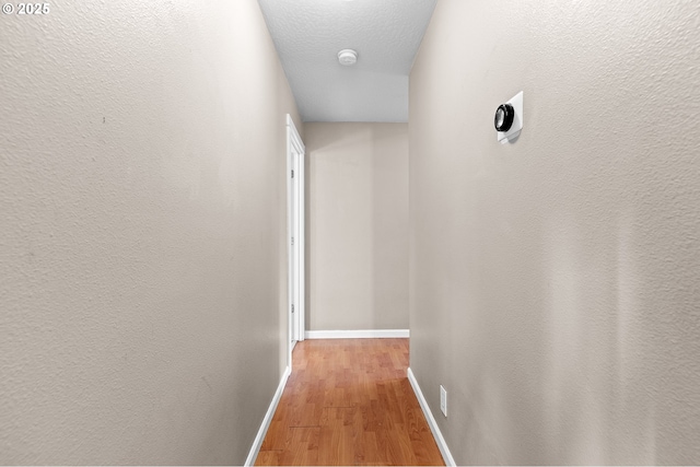 hall with a textured ceiling and light hardwood / wood-style floors