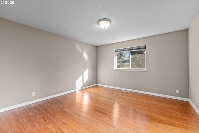 spare room with a textured ceiling and light hardwood / wood-style flooring