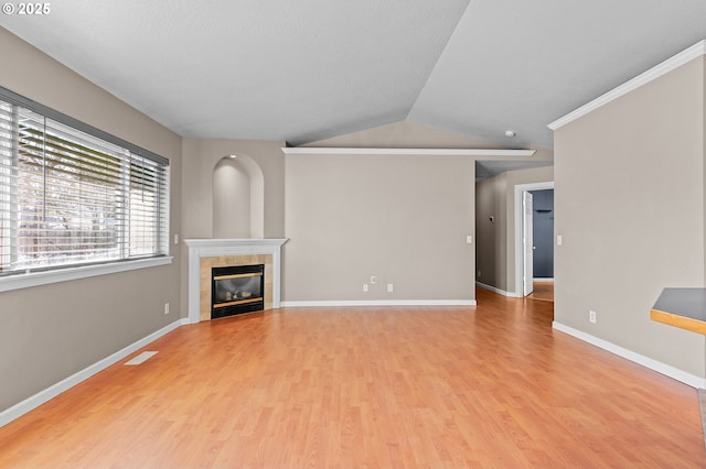 unfurnished living room with a tile fireplace, vaulted ceiling, and light hardwood / wood-style floors