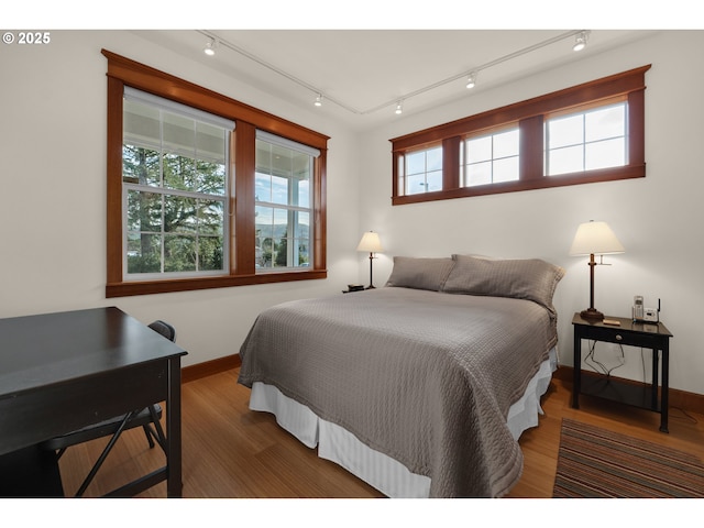 bedroom with track lighting, baseboards, and wood finished floors