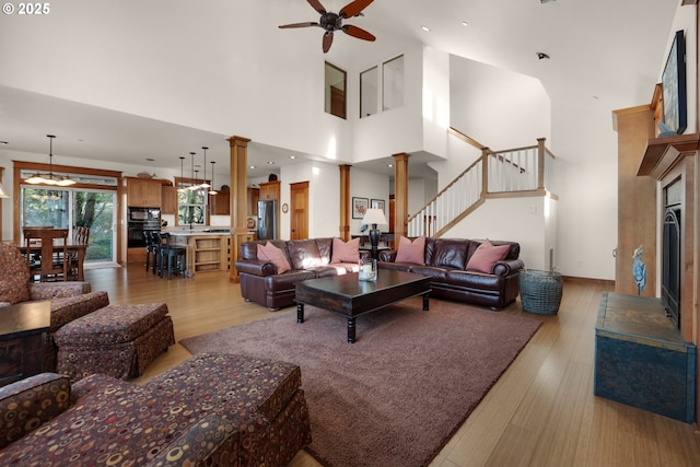 living area featuring a ceiling fan, light wood-type flooring, stairway, a high ceiling, and ornate columns