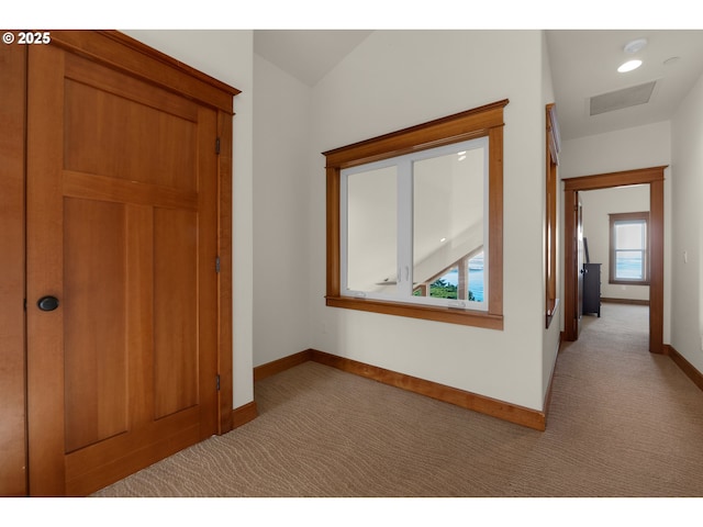 hallway with baseboards, visible vents, and light colored carpet
