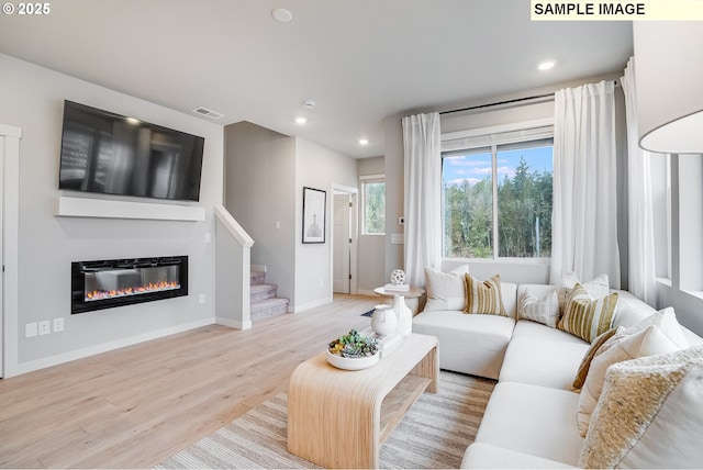 living room with light wood-style flooring, baseboards, a glass covered fireplace, recessed lighting, and stairway